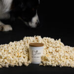 Bougie chien parfumée Oh My Dog par la marque de bougie artisanales parfumées D'Joy, senteur pop corn et caramel, posée à côté d'un chien.